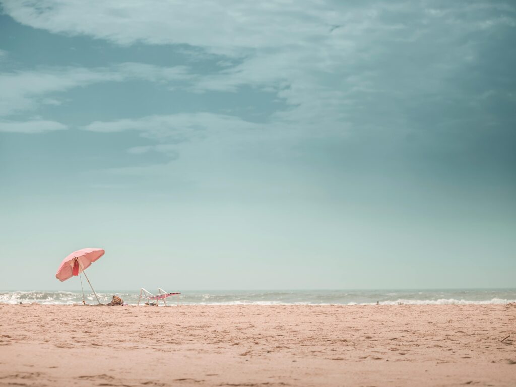 Peaceful beach with pink umbrella and sand, perfect for a summer escape.